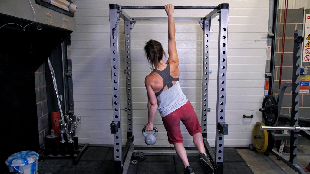 A woman does a one-arm hang holding a kettle bell